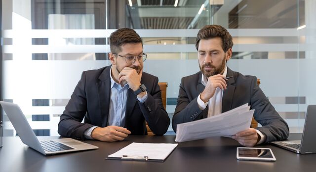 COLOUR-IMAGE_two-men-looking-over-documents-together-at-desk_jul26