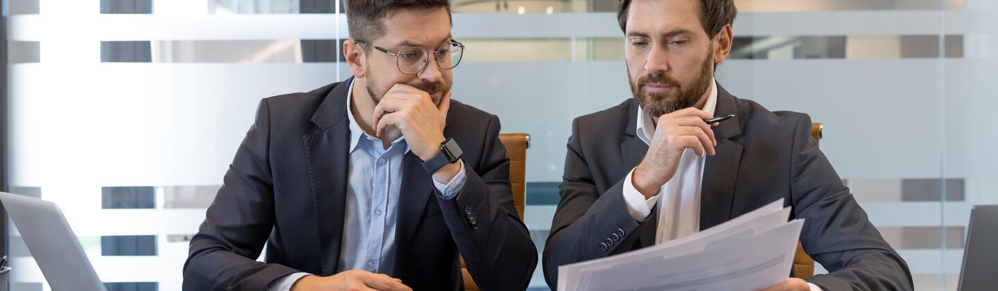 COLOUR-IMAGE_two-men-looking-over-documents-together-at-desk_jul26