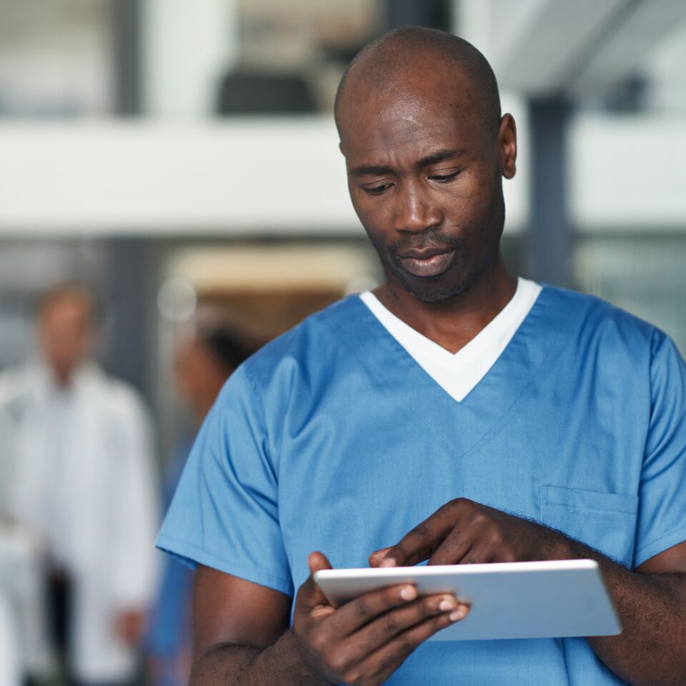 COLOUR-IMAGE_black-male-nurse-using-silver-tablet-in-hallway_apr26