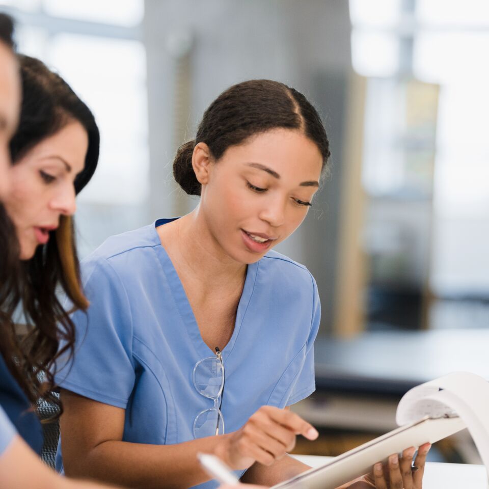 COLOUR-IMAGE_three-nurses-sat-at-desk-looking-through-notes_apr26