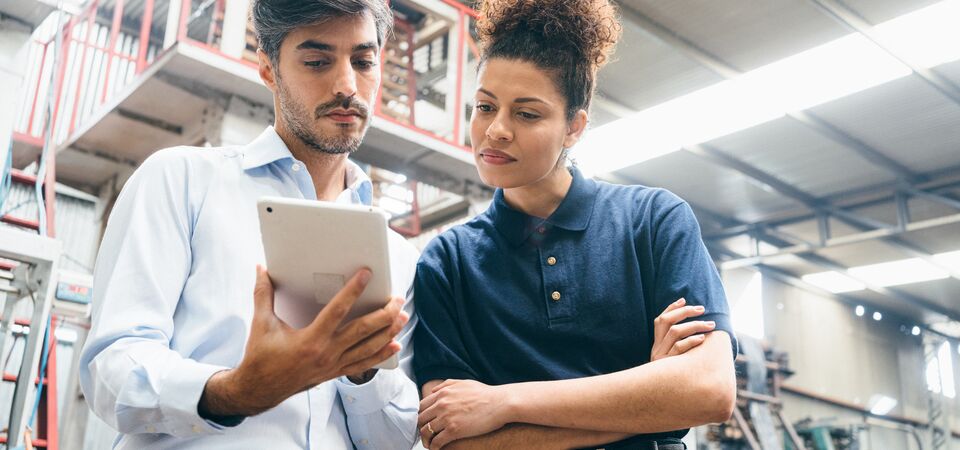 COLOUR-IMAGE_two-colleagues-looking-over-a-tablet-in-factory_apr26