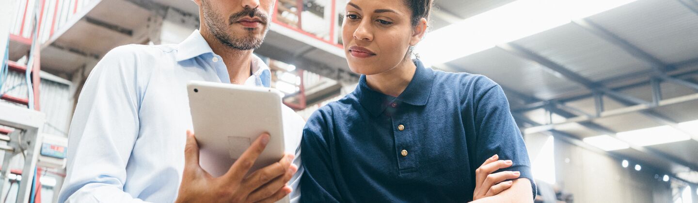 COLOUR-IMAGE_two-colleagues-looking-over-a-tablet-in-factory_apr26