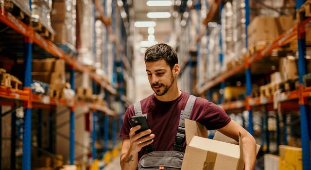 COLOUR-IMAGE_male-warehouse-worker-working-looking-at-mobile-phone_jul26
