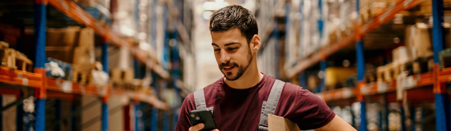 COLOUR-IMAGE_male-warehouse-worker-working-looking-at-mobile-phone_jul26