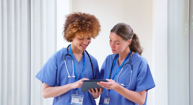 COLOUR-IMAGE_two-female-nurses-using-tablet-wearing-blue-scrubs_apr26
