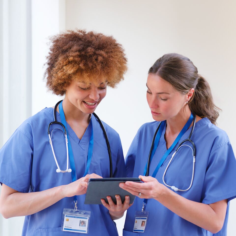 COLOUR-IMAGE_two-female-nurses-using-tablet-wearing-blue-scrubs_apr26