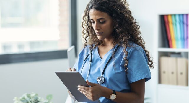 COLOUR-IMAGE_curly-haired-female-nurse-tapping-on-grey-tablet_apr26