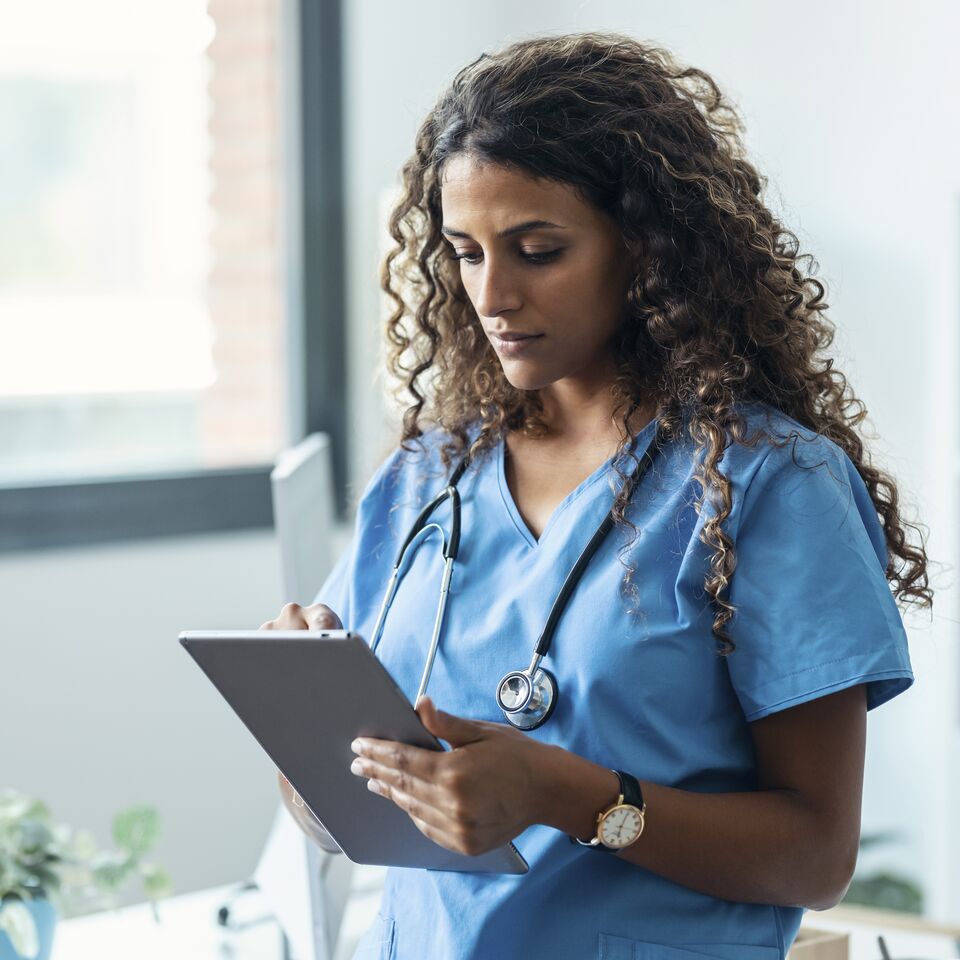 COLOUR-IMAGE_curly-haired-female-nurse-tapping-on-grey-tablet_apr26