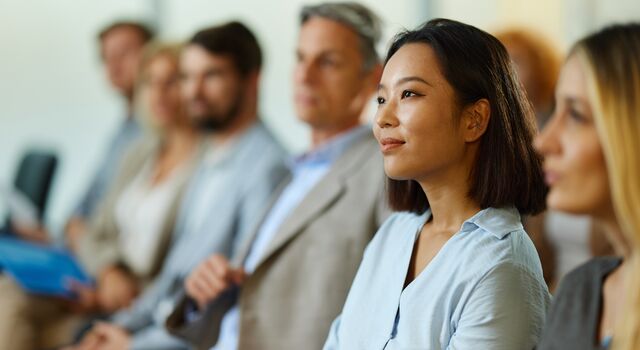 COLOUR-IMAGE_woman-in-conference-audience-smiling-and-engaged_jul26