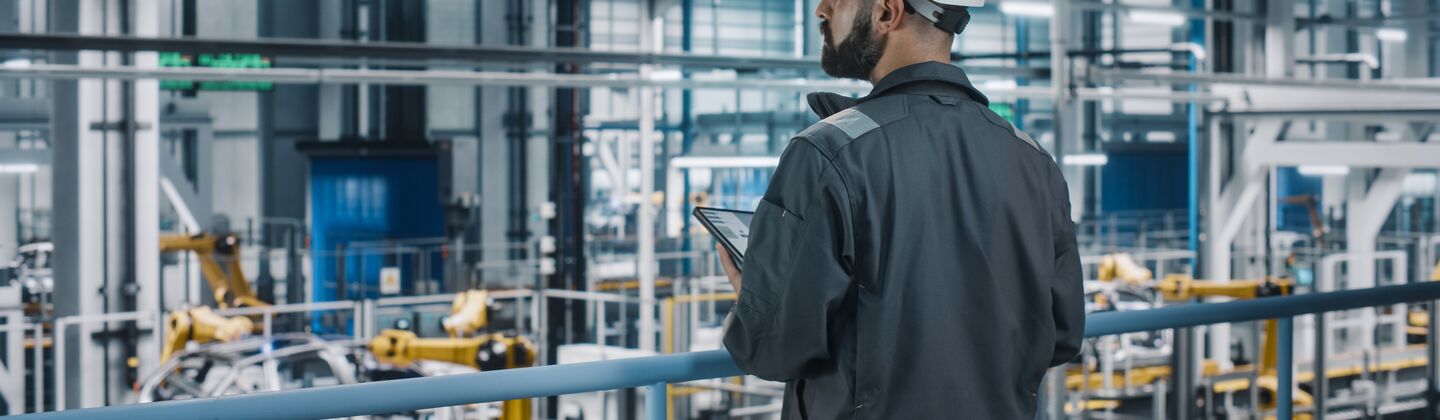 COLOUR-IMAGE_automotive-worker-looking-over-automated-robotic-car-factory-floor-holding-tablet_sep26