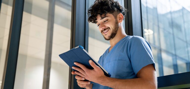 /bynder-asset/bynder:85CA148D-04BA-4D09-8D1BAB63B5765EA7/Landscape_MD/COLOUR-IMAGE_dark-haired-male-nurse-stood-against-window-looking-at-tablet_apr26.jpg?1777555297000