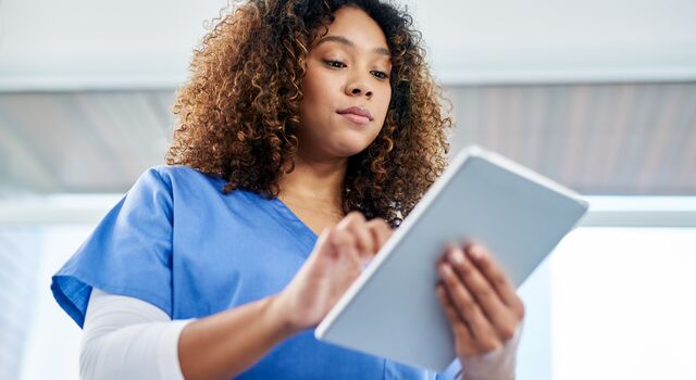 COLOUR-IMAGE_female-nurse-with-brown-curls-using-tablet_apr26