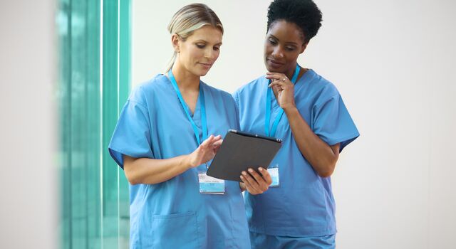 COLOUR-IMAGE_two-female-nurses-with-lanyards-looking-at-tablet-screen_apr26