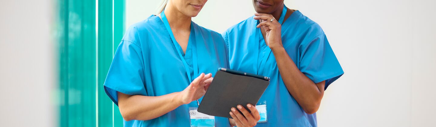 COLOUR-IMAGE_two-female-nurses-with-lanyards-looking-at-tablet-screen_apr26