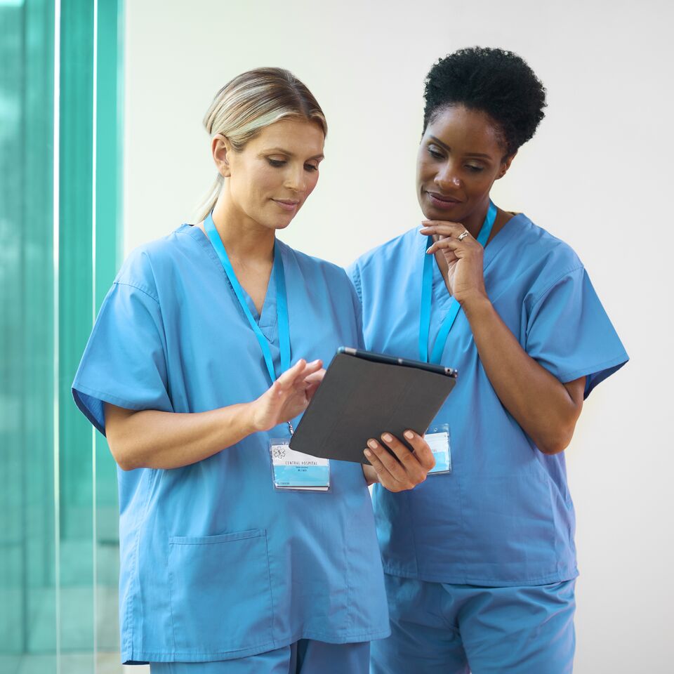 COLOUR-IMAGE_two-female-nurses-with-lanyards-looking-at-tablet-screen_apr26