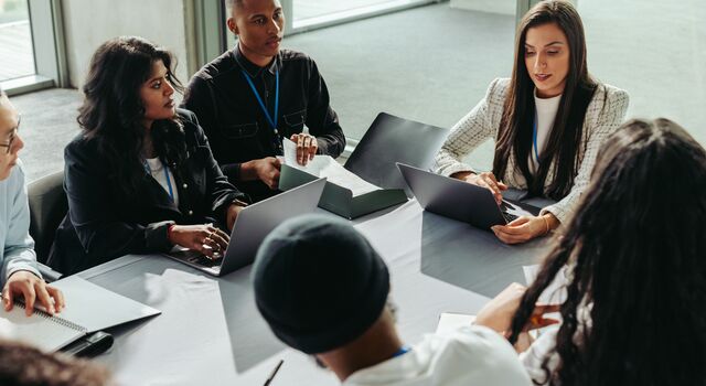 COLOUR-IMAGE_six-professionals-discussing-with-laptops-on-their-table_jul26