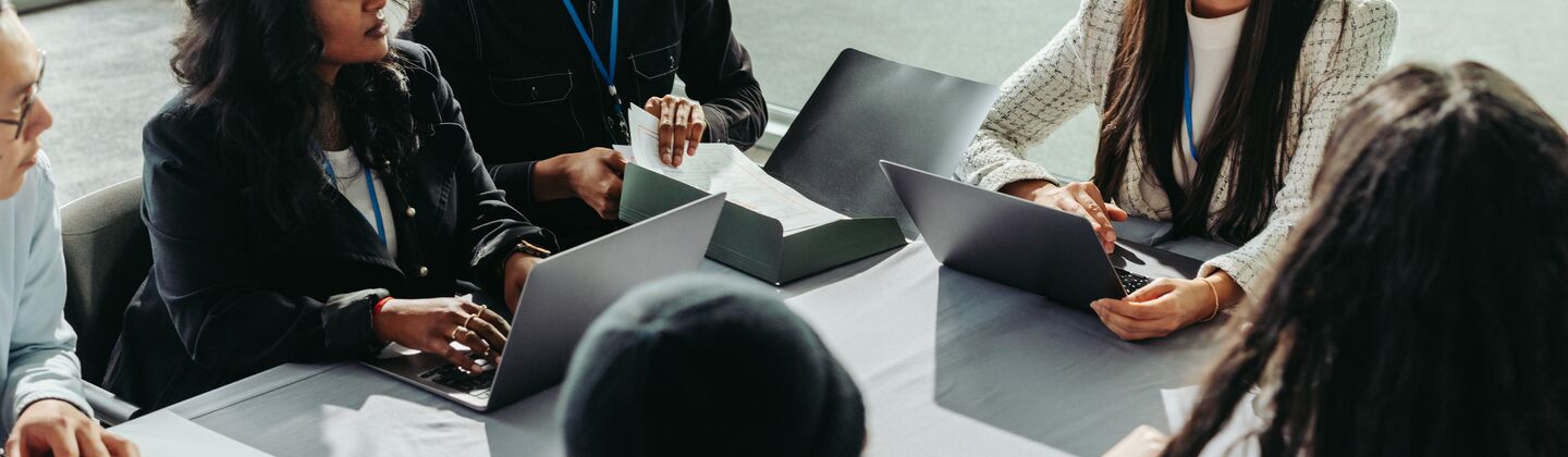 COLOUR-IMAGE_six-professionals-discussing-with-laptops-on-their-table_jul26
