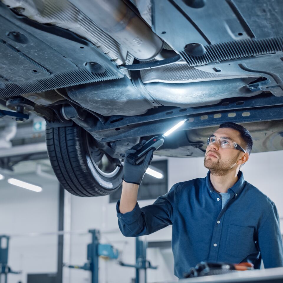 COLOUR-IMAGE_automotive-male-mechanic-shining-light-inspecting-under-car_feb26