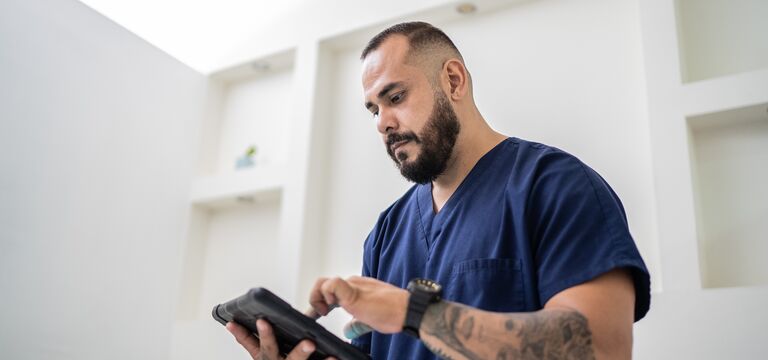 COLOUR-IMAGE_dark-haired-male-nurse-in-navy-scrubs-using-tablet_apr26