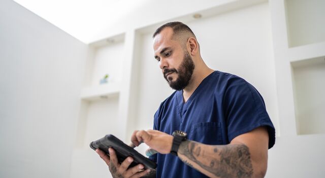 COLOUR-IMAGE_dark-haired-male-nurse-in-navy-scrubs-using-tablet_apr26