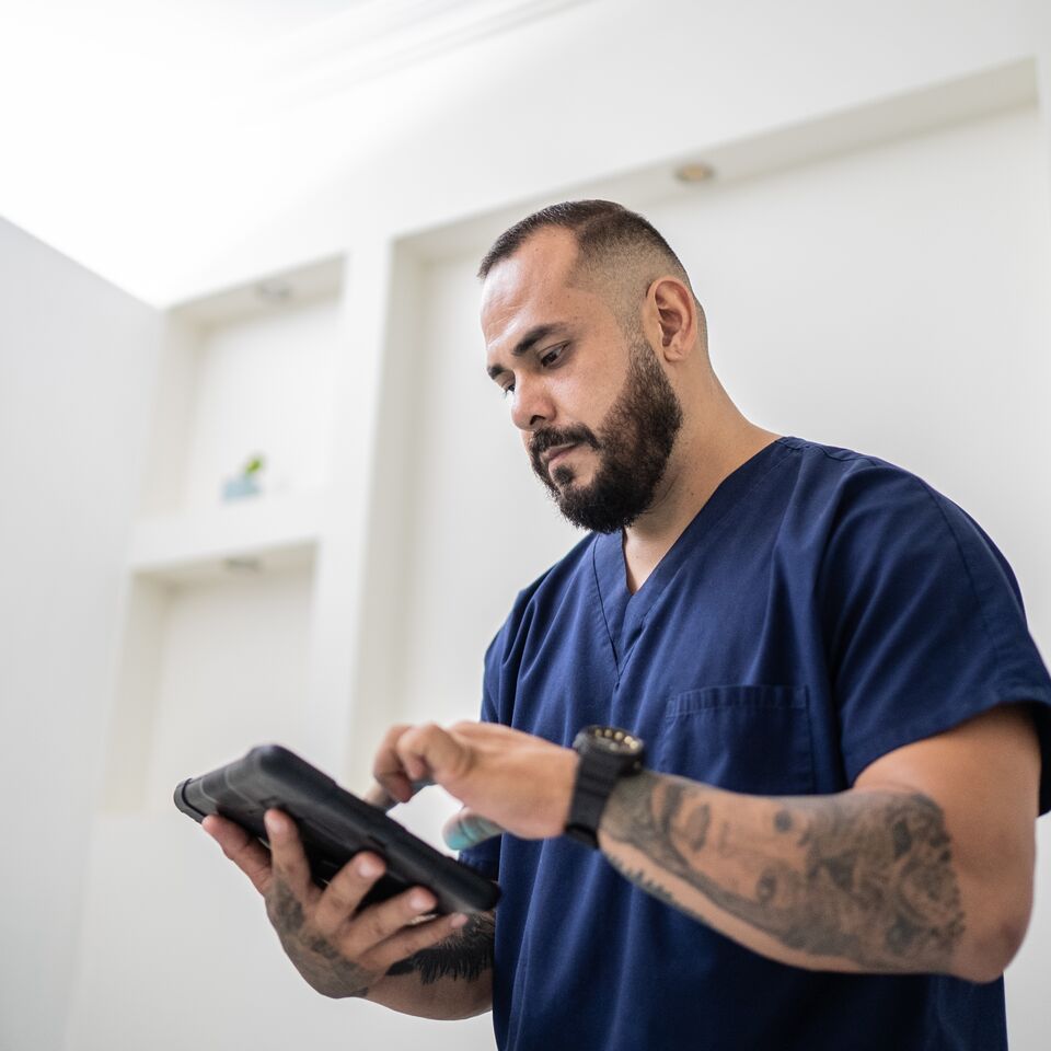 COLOUR-IMAGE_dark-haired-male-nurse-in-navy-scrubs-using-tablet_apr26