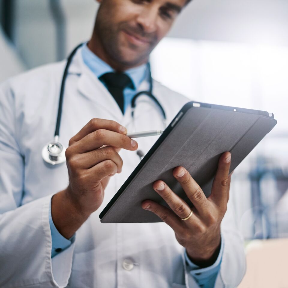 COLOUR-IMAGE_male-doctor-smiling-at-tablet-screen_apr26