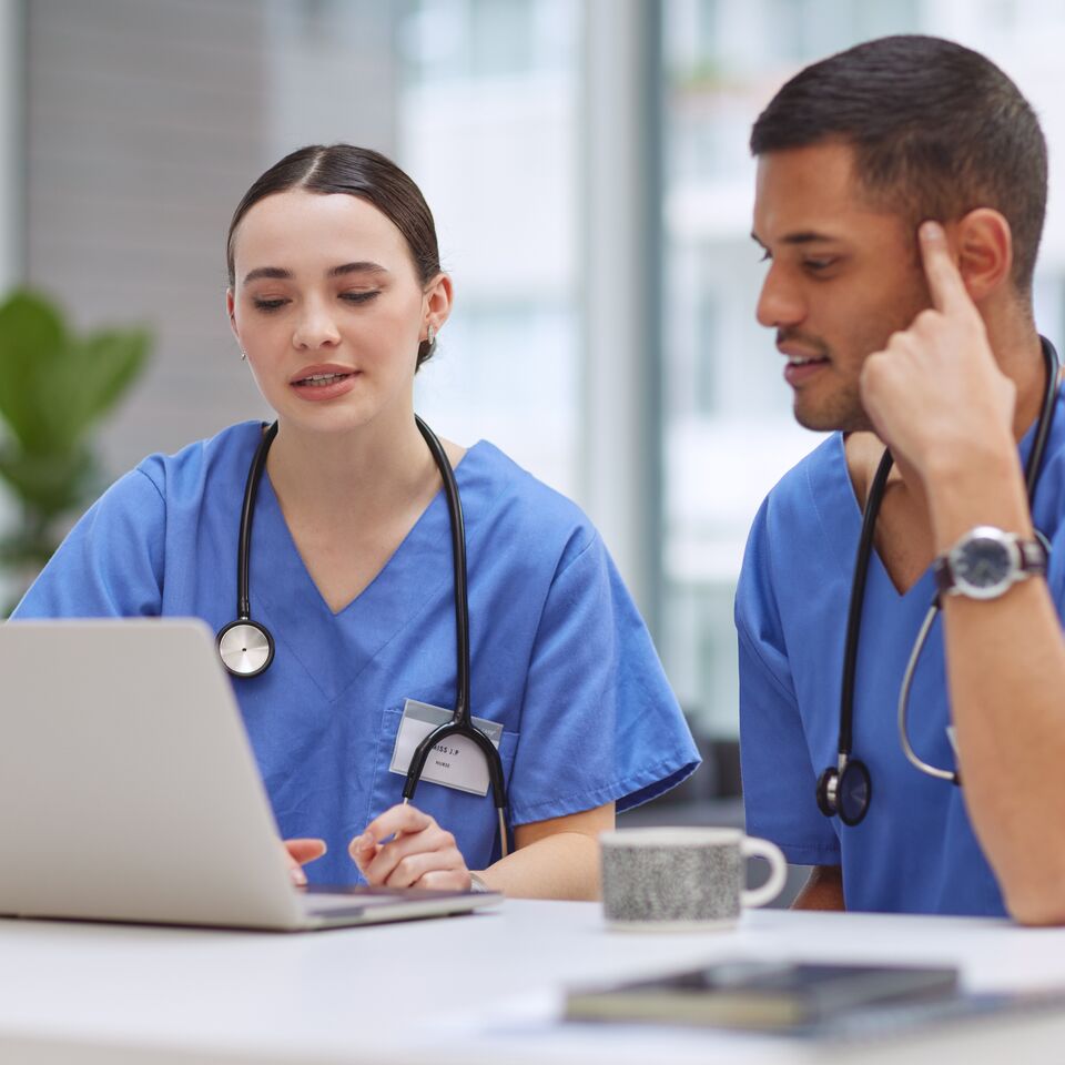 COLOUR-IMAGE_male-and-female-nurses-talking-at-desk-using-laptop_apr26