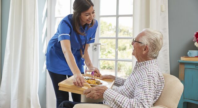 COLOUR-IMAGE_brunette-nurse-smiling-and-caring-for-elderly-patient_apr26