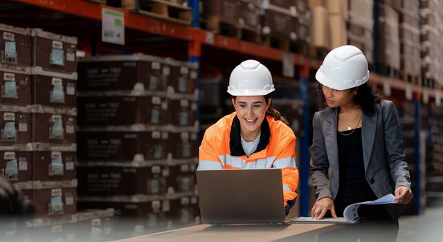 COLOUR-IMAGE-two-female-manufacting-and-supply-chain-workers-with-clipboard-and-laptop-in-warehouse_jul26