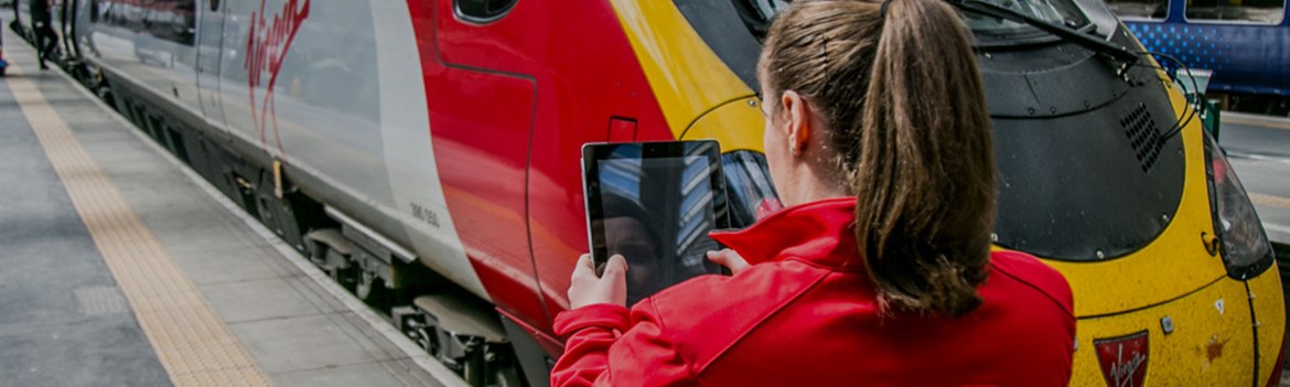 Woman using a tablet next to a red, white and yellow train 